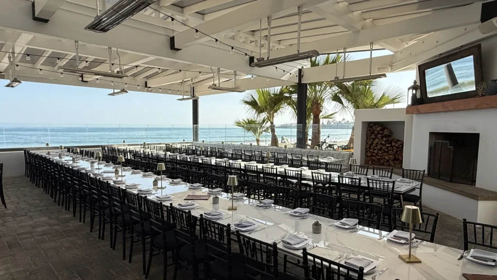 Long group dinner tables set and waiting with the ocean and palms behind them at The Ellwood at Goleta Beach