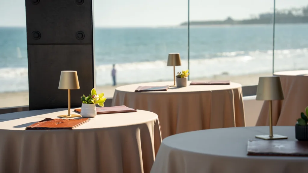 Two blush linen cocktail tables set for a micro wedding reception with the ocean behind at The Ellwood at Goleta Beach